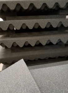 Dark charcoal upside-down egg-crate shaped foam sheets stacked vertically in back, with light gray foam sheets spread horizontally in front.